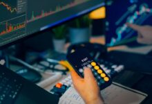 Trader analyzing stock market charts on computer screens with calculator.