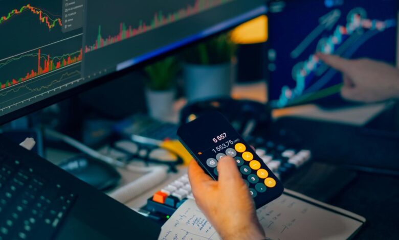 Trader analyzing stock market charts on computer screens with calculator.